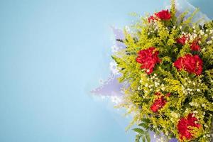 buquê de flores de cravo vermelho com folhas verdes sobre fundo azul foto