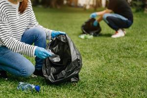 a mão da mulher pega resíduos de plástico para limpeza em saco de reciclagem para limpeza no parque. limpeza, poluição, conceito de ecologia. foto