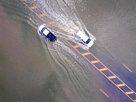 estradas inundadas, pessoas com carros passando. fotografia aérea de drones mostra ruas inundando e carros de pessoas passando, espirrando água. foto