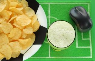 mesa de festa de futebol de futebol com lanches e bebidas. batatas fritas no prato grande pintado como bola de futebol, copo de cerveja, no tapete de prato, vista superior. mouse de computador para assistir partidas transmitidas online. foto