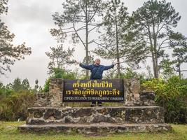 viajante asiático com parabéns ao conquistador de phukradueng sinal no topo do parque nacional de montanha de phu kradueng na cidade de loei tailândia.phu kradueng mountain national park famoso destino de viagem