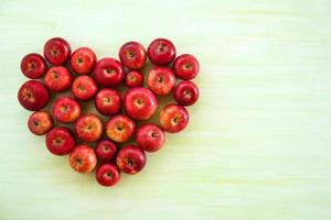 um coração de maçãs vermelhas maduras sobre o fundo verde de madeira, vista superior. foto
