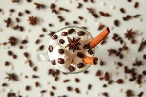 um copo de sorvete com café, paus de canela, grãos de café e estrela de anis no fundo branco. foto