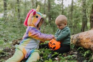 duas crianças andam na floresta com uma cesta de doces de halloween foto