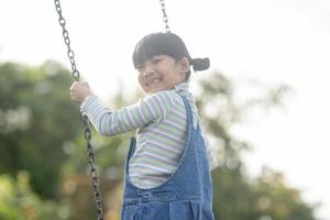 menina asiática feliz jogando balanço ao ar livre no parque foto