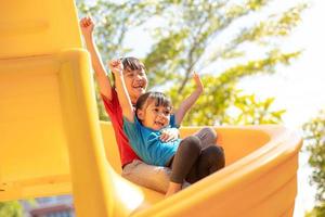 irmãos de meninas bonitinhas se divertindo no playground ao ar livre em dia ensolarado de verão. crianças no slide de plástico. atividade divertida para criança. lazer esportivo ativo para crianças foto