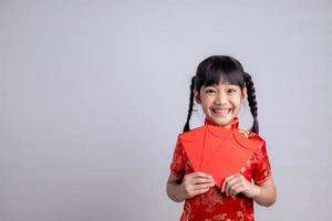 menina asiática feliz no vestido tradicional chinês, sorrindo e segurando um envelope vermelho. feliz ano novo chinês conceito. foto