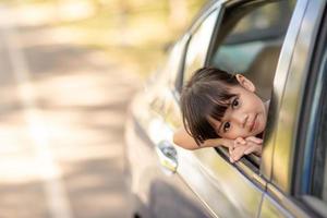 menina asiática bonitinha se divertindo para viajar de carro e olhando pela janela ar na zona rural foto