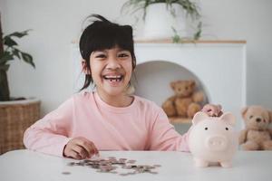 menina asiática economizando dinheiro em um cofrinho, aprendendo sobre economia, criança economizando dinheiro para educação futura. conceito de dinheiro, finanças, seguro e pessoas foto