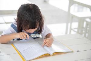 menina asiática lendo os livros na mesa com uma lupa foto