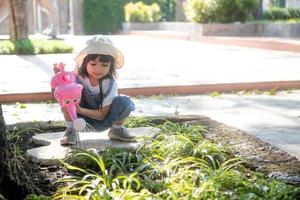 menina asiática despejando água nas árvores. garoto ajuda a cuidar das plantas com um regador no jardim. foto