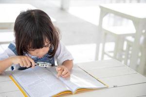 menina asiática lendo os livros na mesa com uma lupa foto