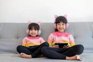 menina de irmãos asiáticos surfando nas redes sociais e jogando no smartphone e tablet digital, e-learning em casa foto