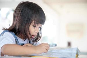 menina asiática lendo os livros na mesa com uma lupa foto