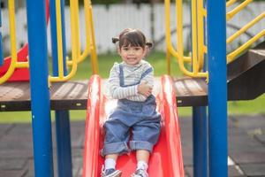 menina criança asiática brincando no playground ao ar livre. as crianças brincam na escola ou no jardim de infância. atividade de verão saudável para crianças. foto