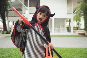 menina criança asiática em fantasia de demônio segurando tridente preto e vermelho, conceito de feliz dia das bruxas
