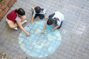 crianças asiáticas brincam ao ar livre. menina criança desenha um globo do planeta com um mapa do mundo colorido giz na calçada, asfalto. terra, concerto do dia da paz. foto