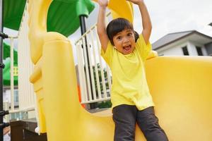 criança brincando no playground ao ar livre. as crianças brincam na escola ou no jardim de infância. criança ativa no escorregador colorido e balanço. atividade de verão saudável para crianças. foto