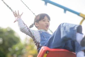 menina asiática feliz jogando balanço ao ar livre no parque foto