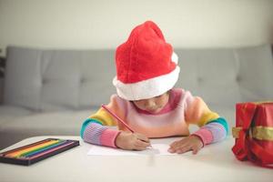 criança de natal escreve carta para papai noel, criança com chapéu de papai noel escrevendo lista de desejos foto