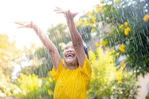 menina asiática feliz se divertindo para brincar com a chuva à luz do sol foto