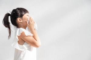 menina criança asiática doente com espirros no nariz e tosse fria em papel de seda porque fraco ou vírus e bactérias do clima de poeira foto
