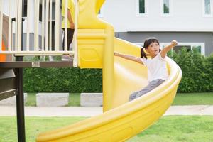 criança brincando no playground ao ar livre. as crianças brincam na escola ou no jardim de infância. criança ativa no escorregador colorido e balanço. atividade de verão saudável para crianças. foto