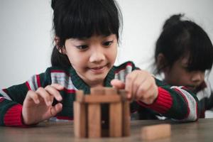 menina asiática alegre brincando com blocos de madeira. se divertindo e aprendendo a criatividade. conceito de criança inteligente. foto