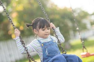 menina asiática feliz jogando balanço ao ar livre no parque foto