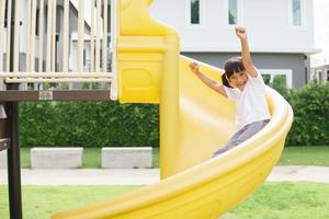 criança brincando no playground ao ar livre. as crianças brincam na escola ou no jardim de infância. criança ativa no escorregador colorido e balanço. atividade de verão saudável para crianças. foto