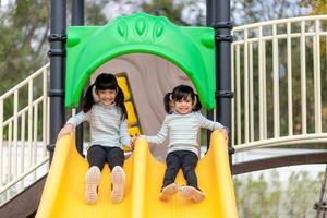 criança brincando no playground ao ar livre. as crianças brincam na escola ou no jardim de infância. criança ativa no escorregador colorido e balanço. atividade de verão saudável para crianças. foto