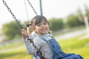 menina asiática feliz jogando balanço ao ar livre no parque foto