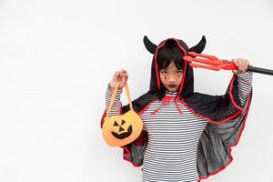 menina criança asiática em fantasia de demônio segurando tridente preto e vermelho, conceito de feliz dia das bruxas foto