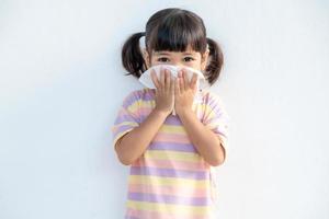 menina criança asiática doente com espirros no nariz e tosse fria em papel de seda porque fraco ou vírus e bactérias do clima de poeira e jardim de infância e pré-escola foto
