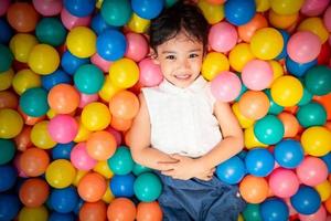 menina asiática feliz jogando na piscina de bolas coloridas foto
