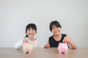 duas meninas asiáticas se divertindo para colocar moedas no cofrinho juntos, garoto economizando dinheiro para o futuro conceito foto