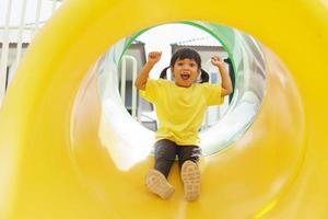 criança brincando no playground ao ar livre. as crianças brincam na escola ou no jardim de infância. criança ativa no escorregador colorido e balanço. atividade de verão saudável para crianças. foto