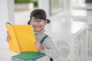 menina asiática feliz lendo um livro em cima da mesa foto