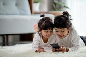 irmãos asiáticos juntos no chão usando smartphone foto