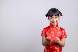 menina asiática feliz no vestido tradicional chinês, sorrindo e segurando um envelope vermelho. feliz ano novo chinês conceito. foto