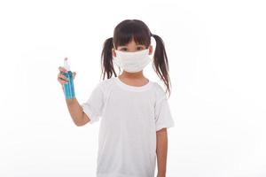 linda garota asiática usando uma máscara e lavando as mãos com álcool para evitar a propagação da doença em um fundo branco. prevenção da propagação do vírus da gripe coronariana covid-19 influenza foto