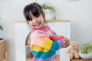 menina asiática sorri e animado e segurando a caixa de presente vermelha no fundo da sala de estar. criança segurando a caixa de presente no natal e ano novo. sorriso e surpresa da menina da criança asiática. foto