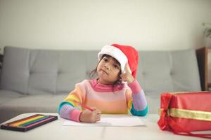 criança de natal escreve carta para papai noel, criança com chapéu de papai noel escrevendo lista de desejos foto