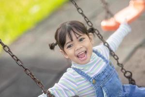 menina asiática feliz jogando balanço ao ar livre no parque foto