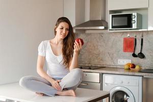 linda mulher caucasiana casual está prestes a morder uma maçã na cozinha, uma jovem foto