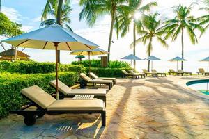 lindo guarda-sol de luxo e cadeira ao redor da piscina externa em hotel e resort com coqueiro no céu azul foto