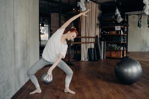 bailarina jovem ruiva magra fazendo plie com fitball pequeno na mão foto