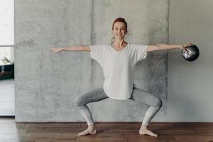 esbelta senhora ruiva feliz sentada em plie durante o treino de barre no ginásio foto