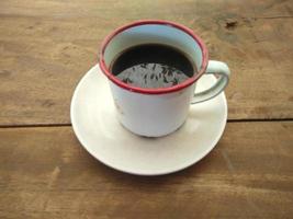 uma xícara de café preto sentado em uma mesa feita de tábuas de madeira foto