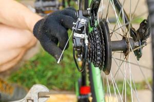 homem mecânico de bicicleta repara bicicleta na oficina de bicicletas, ao ar livre. mão de ciclista examina, corrige o sistema de transmissão de ciclo moderno. manutenção de bicicletas, conceito de loja de esportes. foto